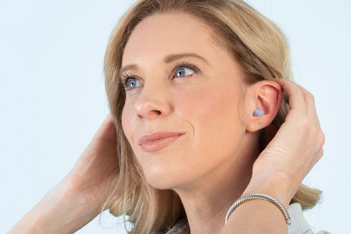 Picture of a woman with EarPlanes earplugs in her ear looking off into the distance.
